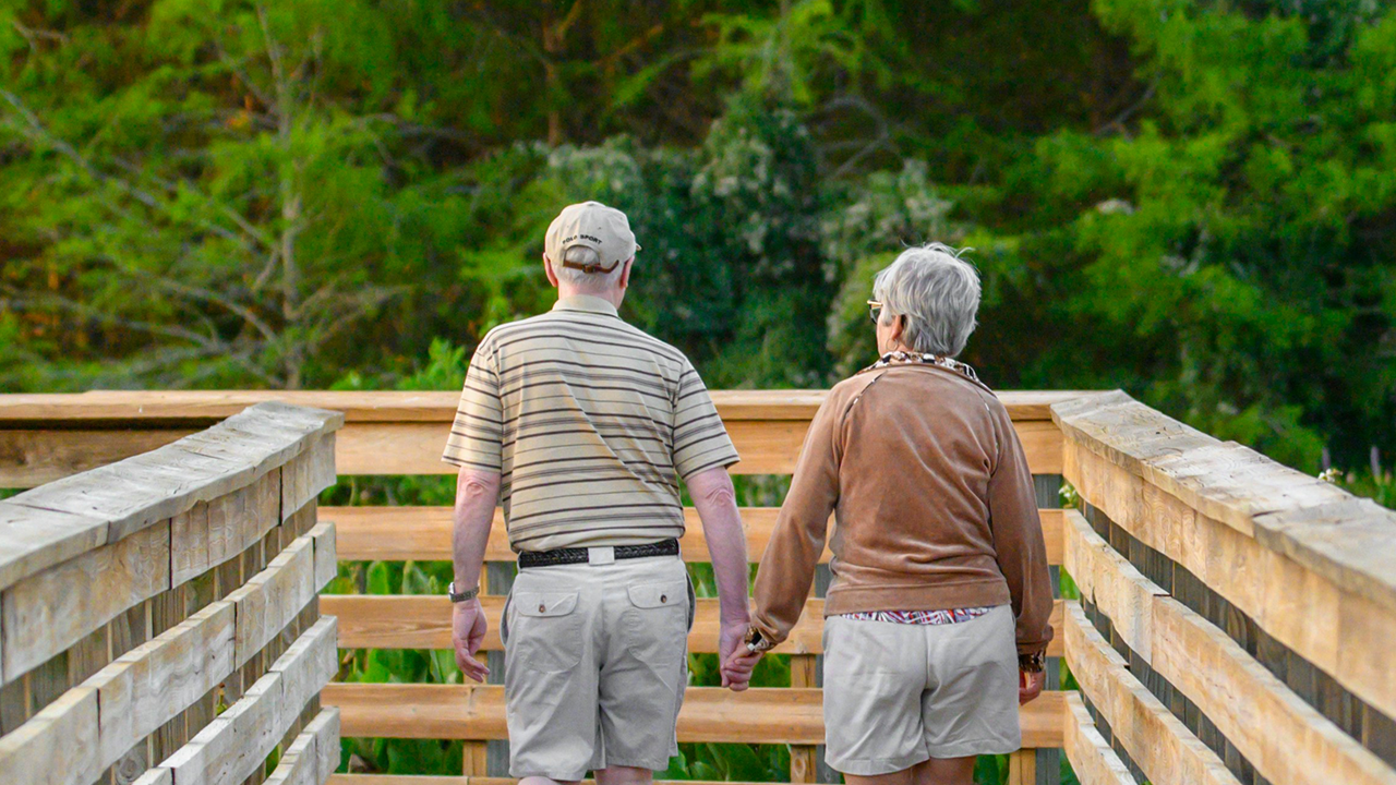 An image of a senior couple retiring in Oakville on a walk along the boardwalk in the summer.
