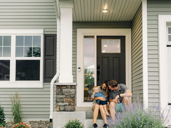 An Oakville couple who have recently purchased a home in Oakville with their baby and them sitting at the front of the house.