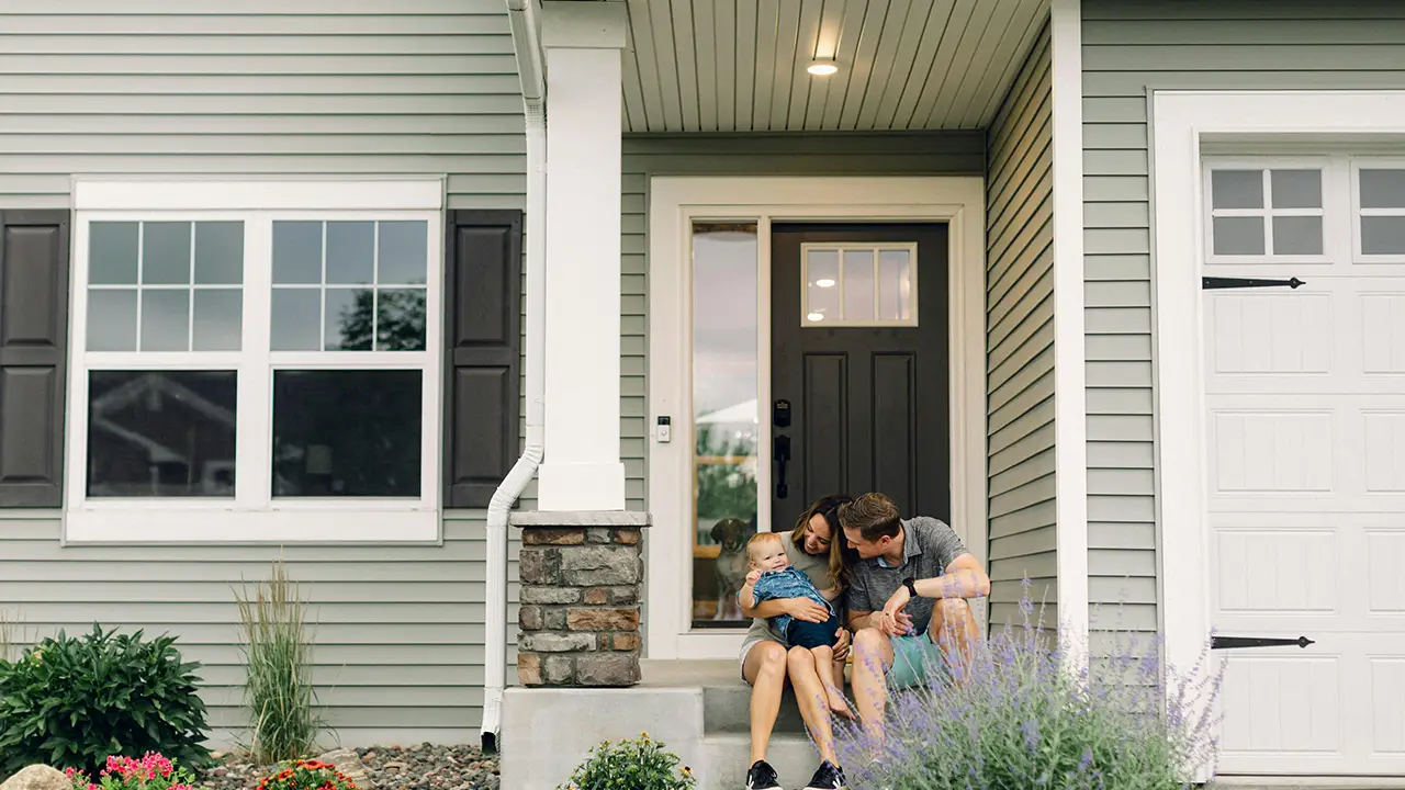An Oakville couple who have recently purchased a home in Oakville with their baby and them sitting at the front of the house.